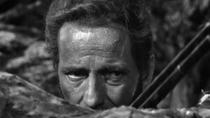 Humphrey Bogart peaking over a rock with a rifle in Treasure of the Sierra Madre